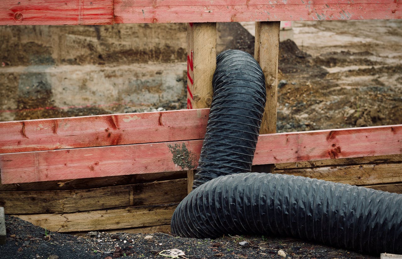 Close-up of a construction site showing red wooden barriers and a flexible black duct.